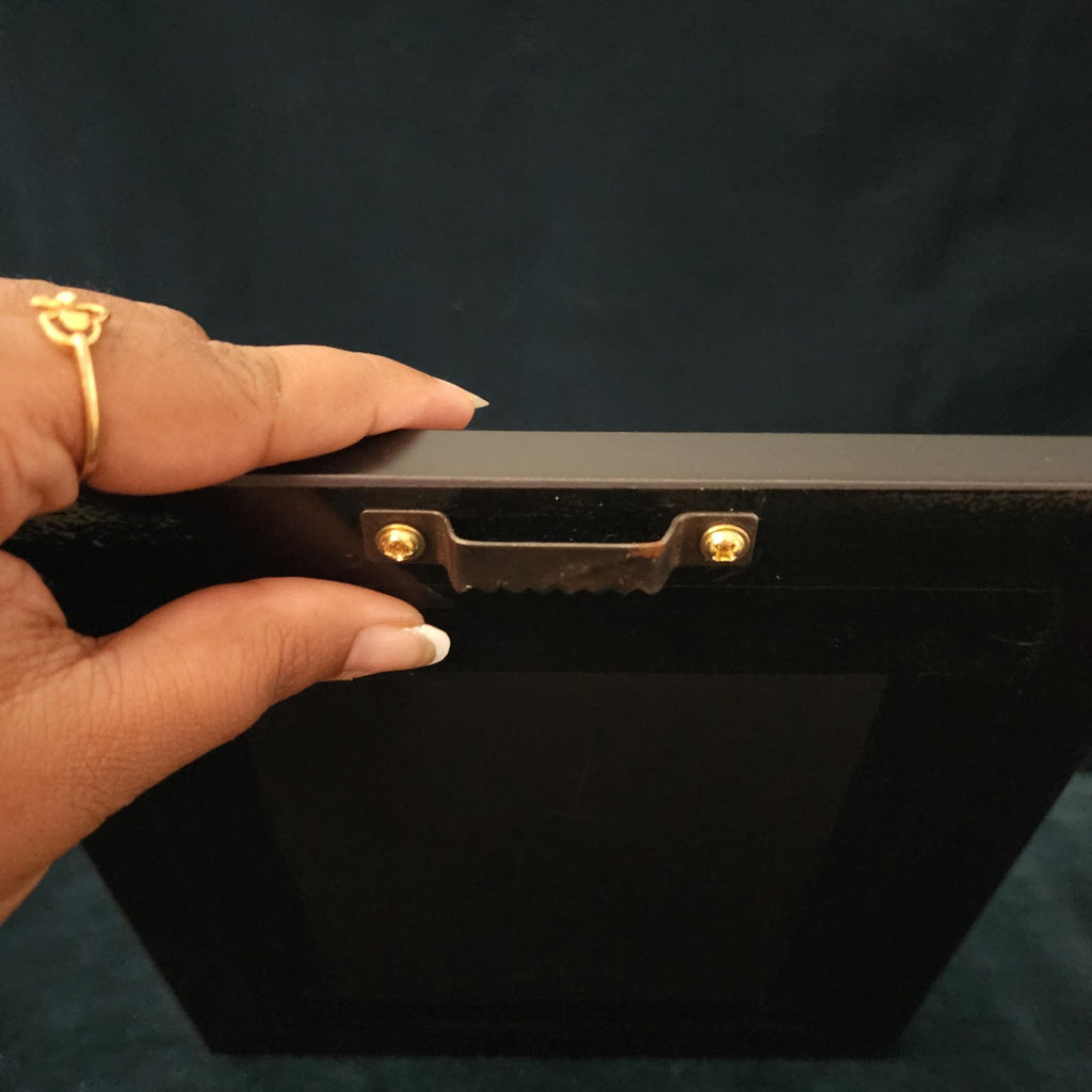 Hand holding a black rectangular object with gold accents against a dark background