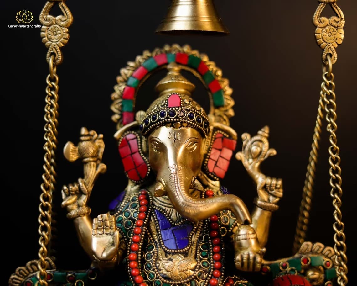Decorative Ganesh statue on a swing with intricate gold and colored stone detailing.