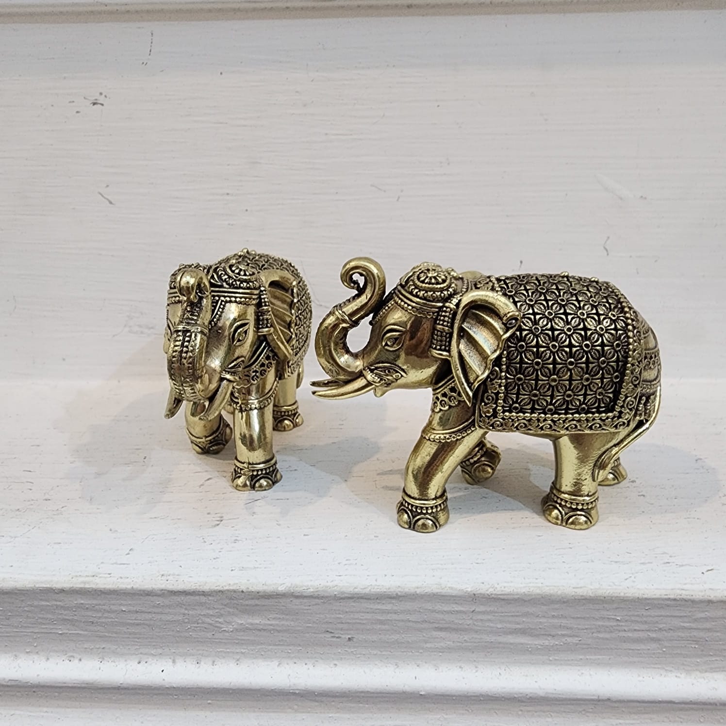 Two ornate brass elephants on a white surface