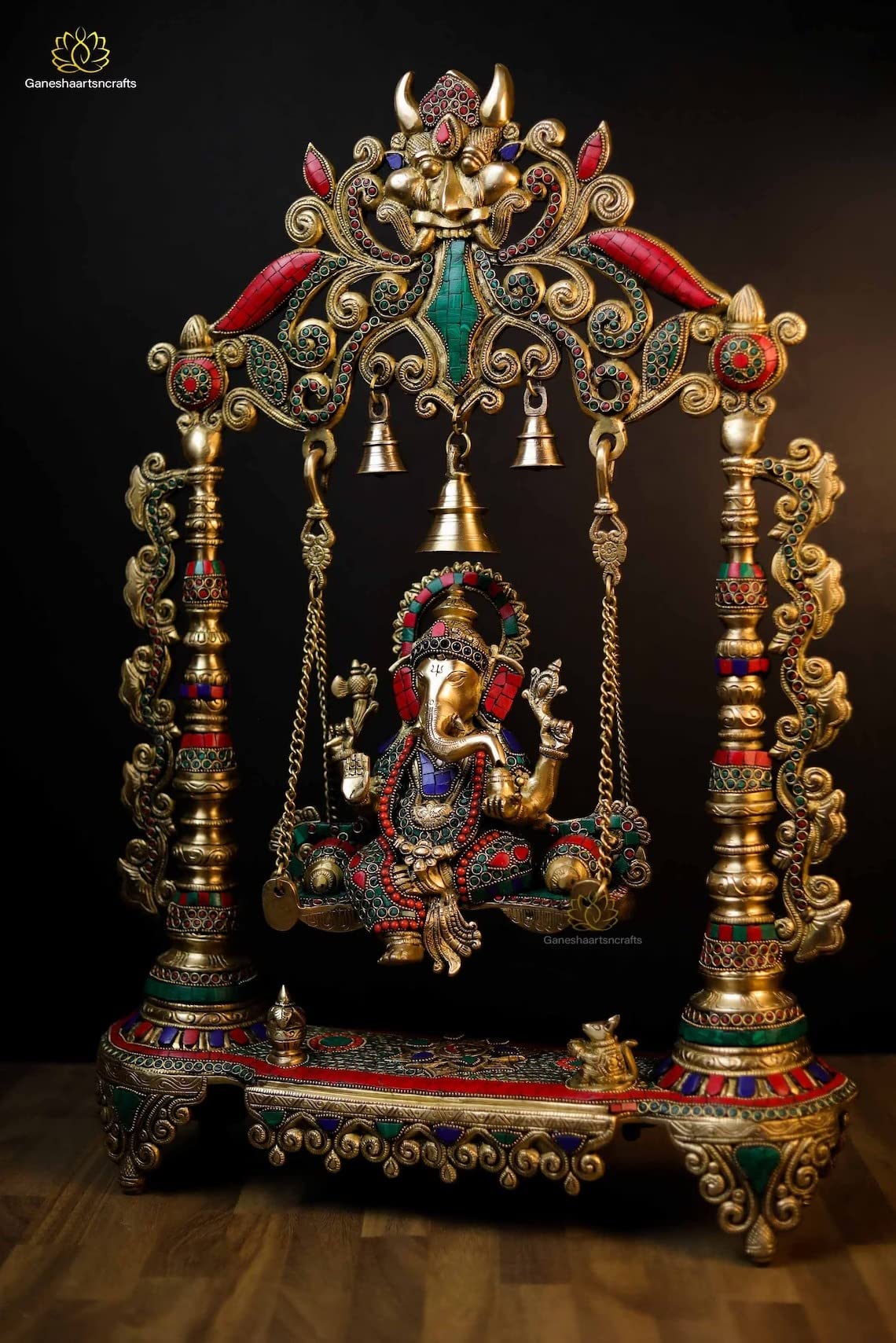 Decorative Ganesh statue on a swing with intricate gold and colored stone detailing.