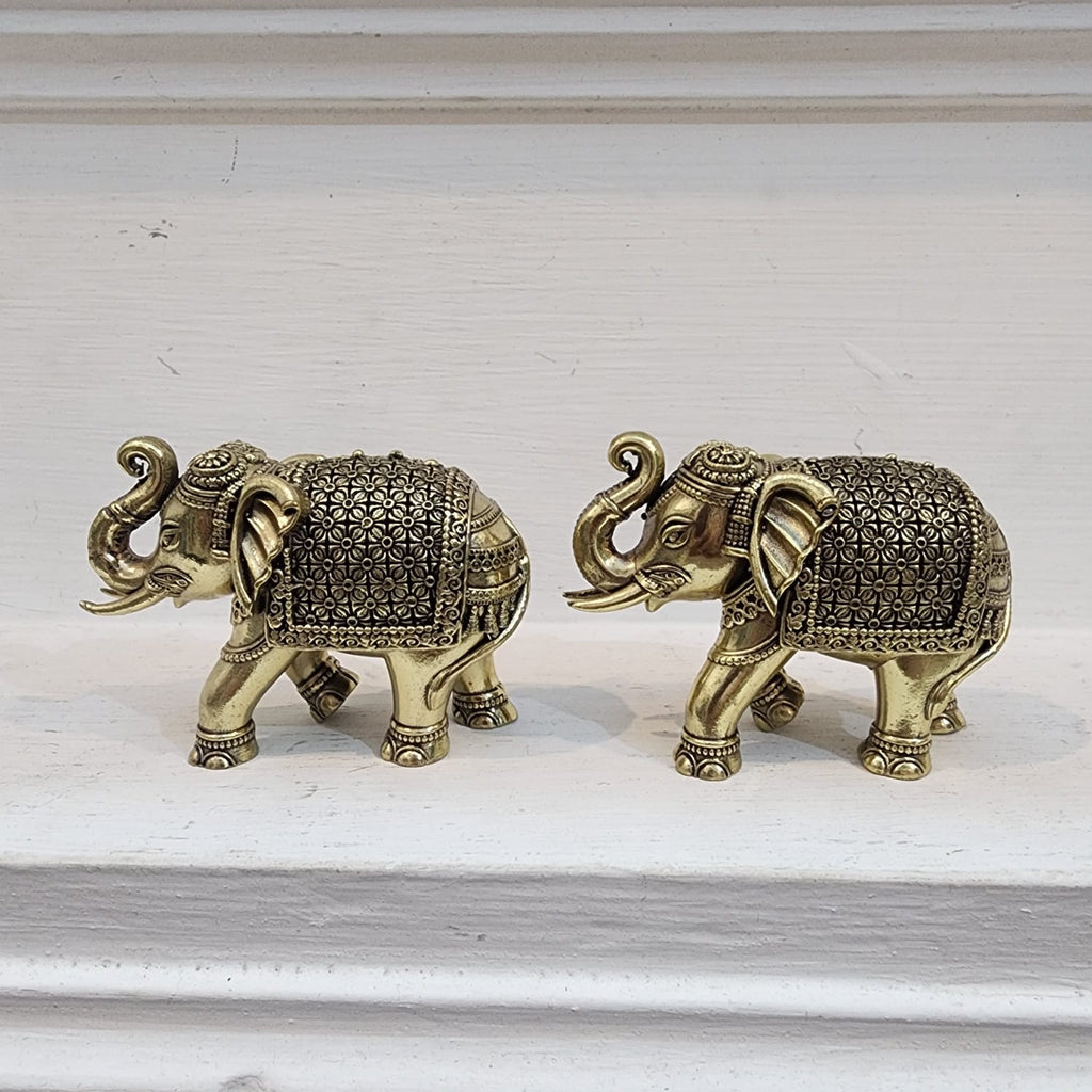 Two ornate brass elephant figurines on a light wooden surface.