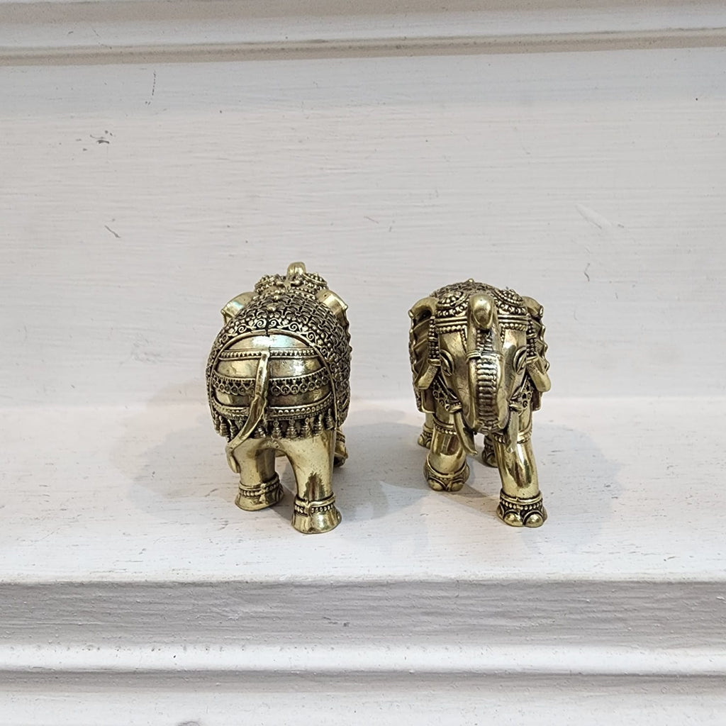 Two ornate brass elephants on a white surface