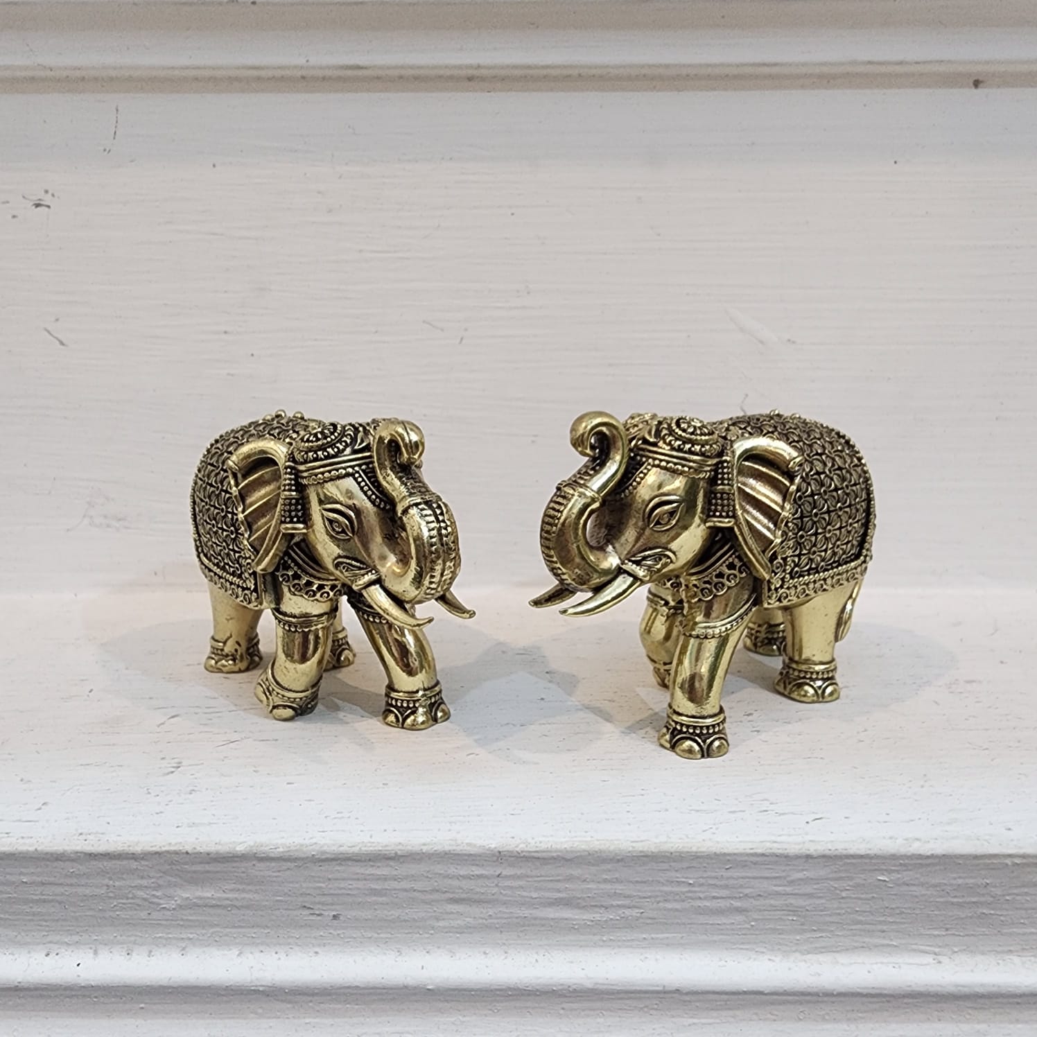 Two ornate brass elephant figurines on a light wooden surface.