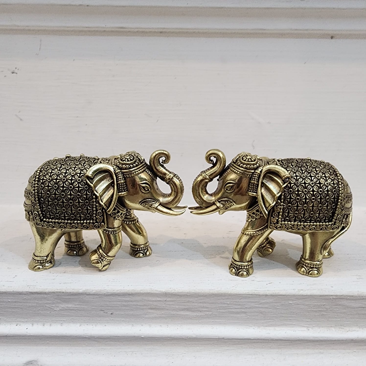 Two ornate brass elephants on a white surface