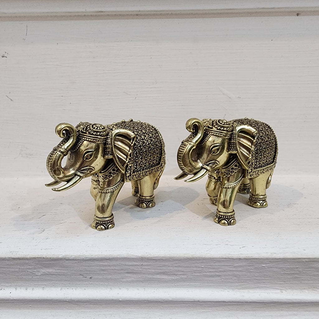 Two ornate brass elephant figurines on a white surface.