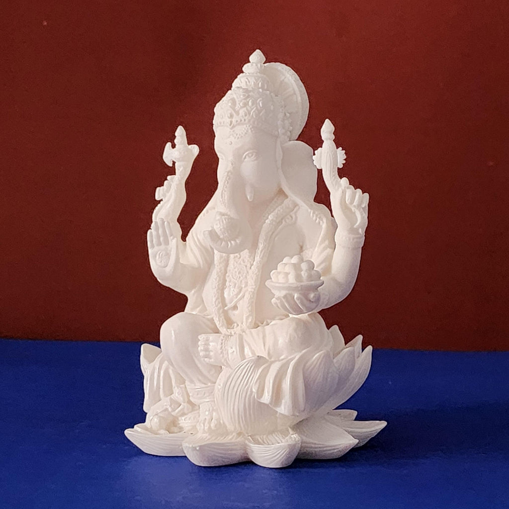 White statue of a deity sitting on a lotus flower against a red and blue background