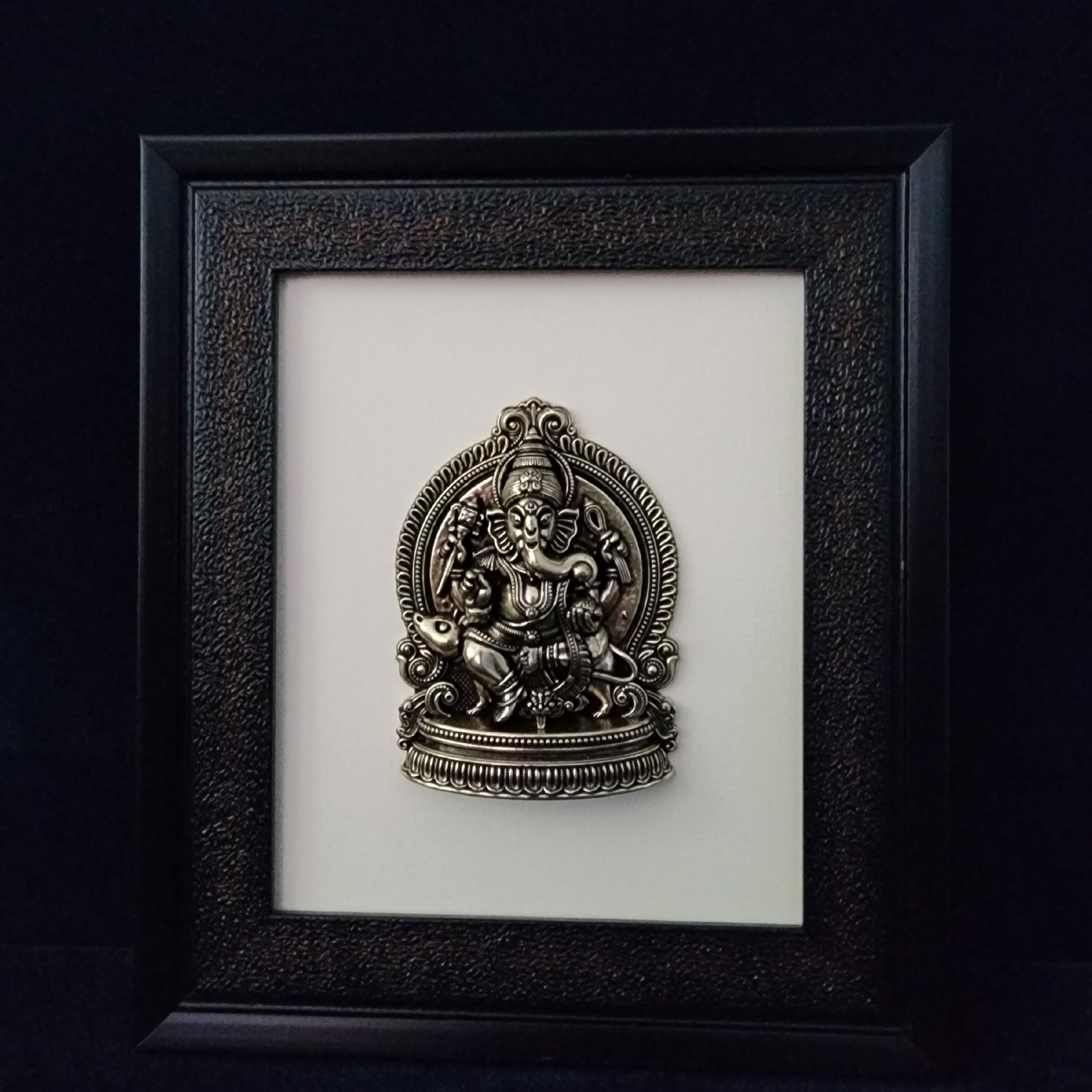 Decorative metal sculpture of a deity in a black frame on a white background