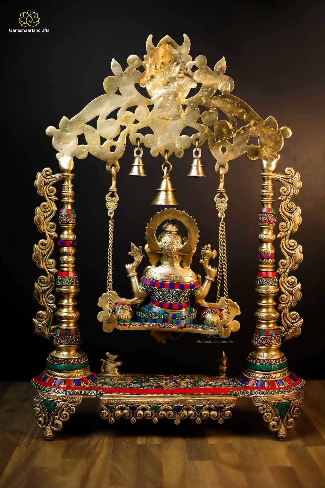 vDecorative Ganesh statue on a swing with intricate gold and colored stone detailing.